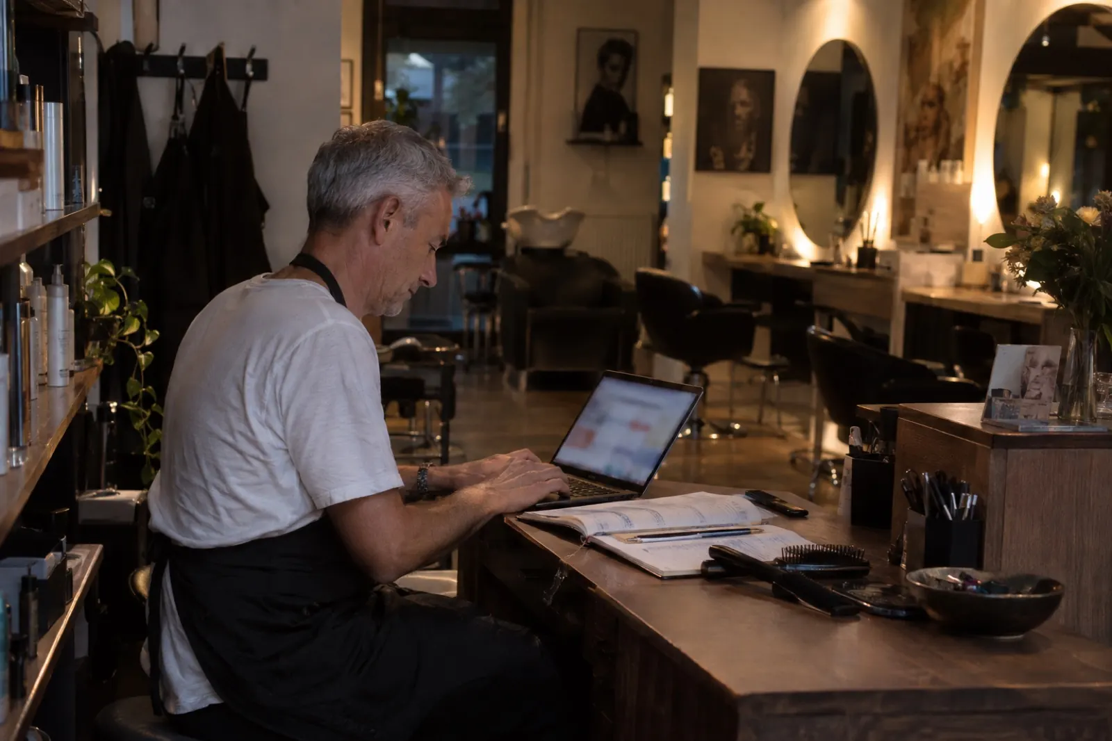 Friseur arbeitet nach Feierabend am Empfangstresen seines Salons am Laptop