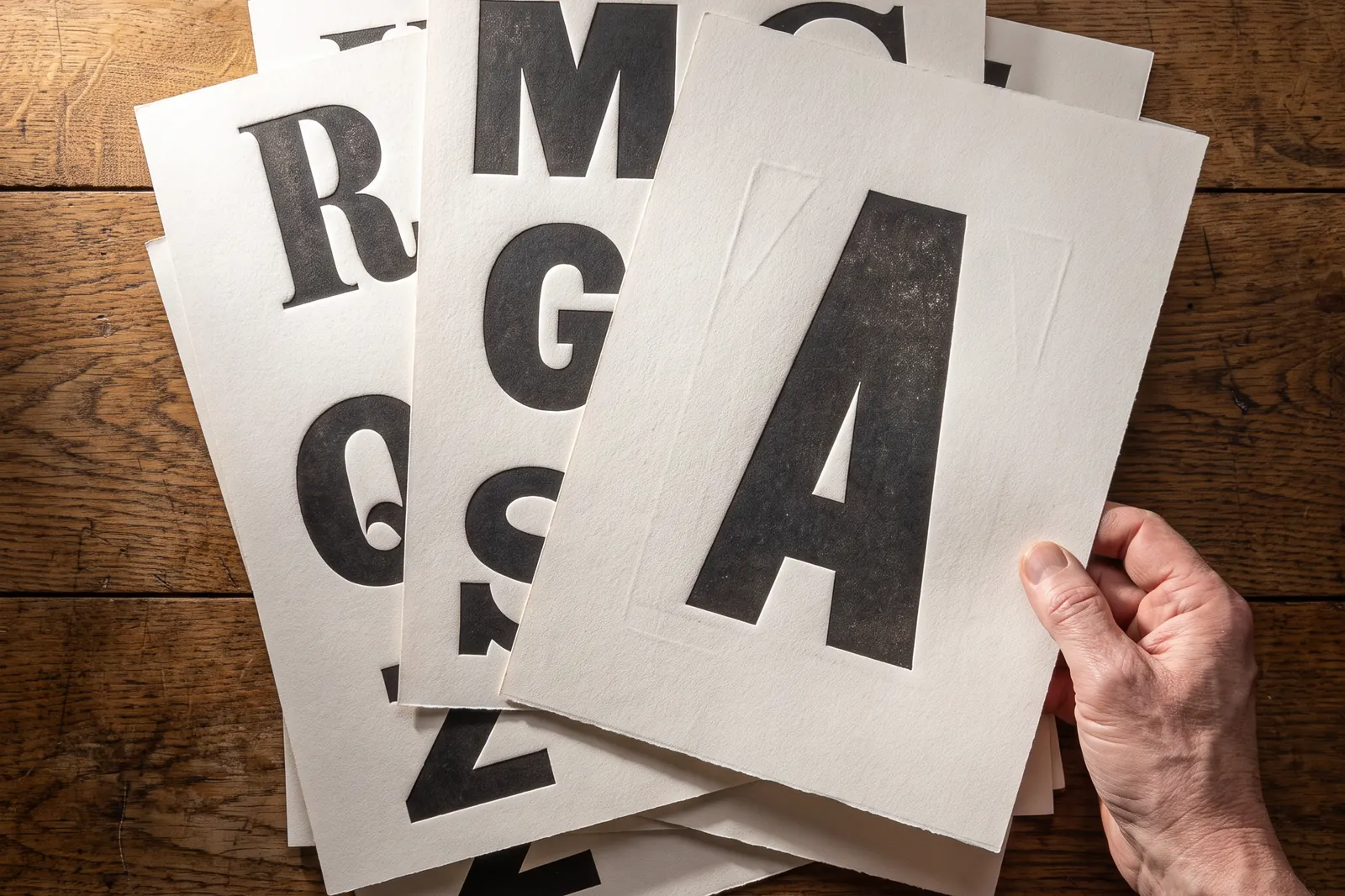 Hand blättert durch Bögen mit großen gedruckten Buchstaben verschiedener Schriftarten